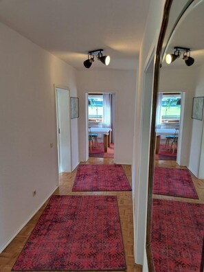 A hallway with a red carpet leading to a dining area with a table and chairs.