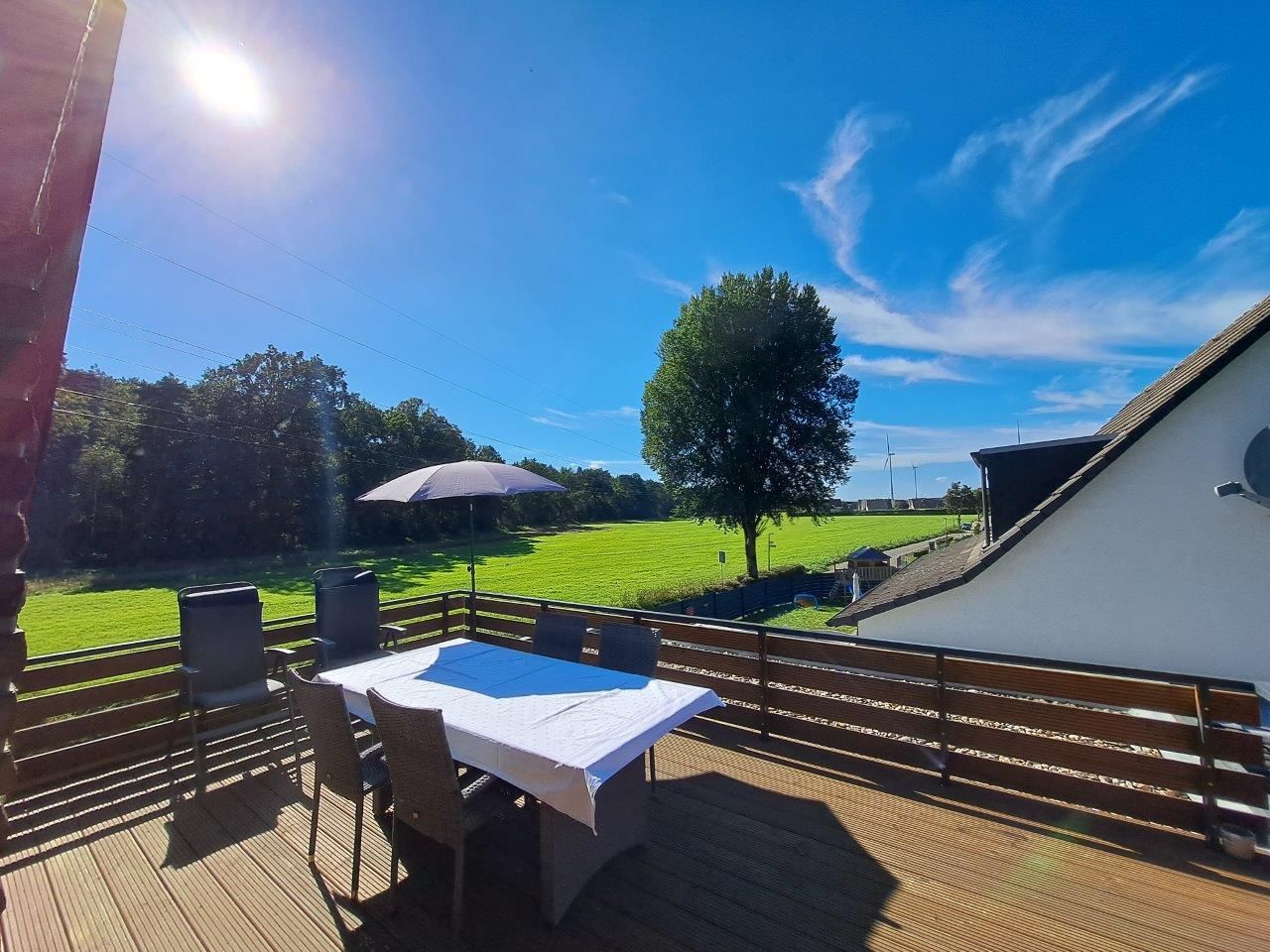 An outdoor deck with a table and chairs, a view of a green field, and a building in the background.