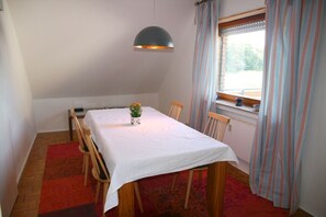 Un comedor con una mesa dispuesta para cuatro personas, una lámpara colgante, una ventana con cortinas y un radiador.