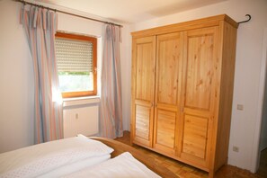 A bedroom with a bed, a window with curtains, and a wooden wardrobe.