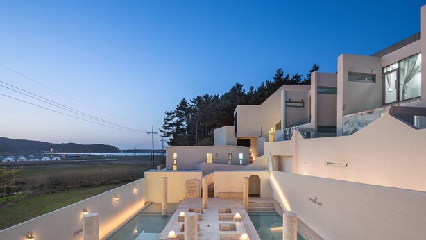 Un área de piscina moderna con un elemento acuático central, rodeada de columnas iluminadas y una vista despejada del paisaje.