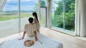 Un dormitorio con una cama grande, vistas a la vegetación y un paisaje urbano a través de las ventanas.
