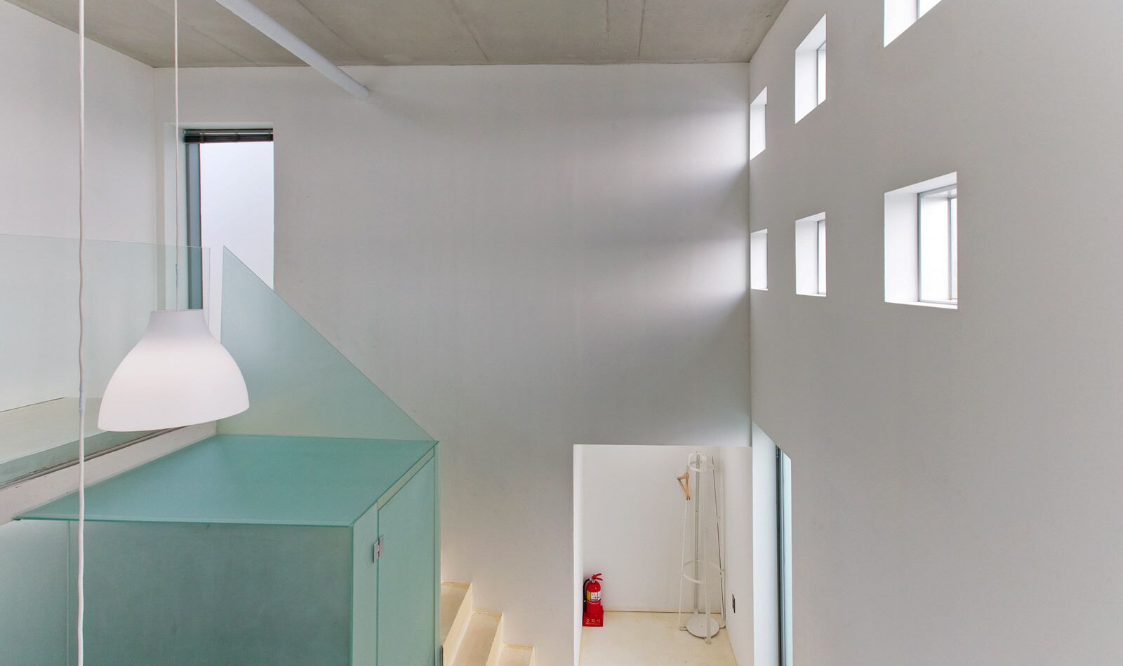 A modern interior with a staircase, a hanging light fixture, and a visible fire extinguisher.