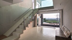 Un interior moderno con una escalera que lleva a un balcón, ventanas amplias que ofrecen vistas al exterior y un ventilador de techo.