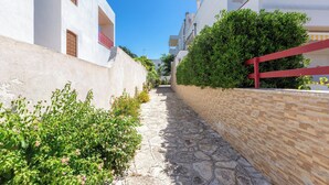 Une ruelle étroite, pavée de pierres, bordée de bâtiments aux murs blancs et aux balcons rouges.