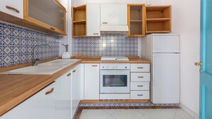 Une cuisine compacte avec des meubles blancs, un four encastré, un évier et un réfrigérateur.