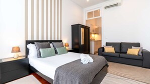 A modern hotel room with a large bed, a sofa, a wardrobe, and a kitchenette. - Charming Studio w/ Balcony, A/C and Kitchen (Porto)
