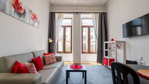 A living room with a sofa, a small table, a TV, and a window with curtains. - Cozy Studio Central Porto: A/C and Kitchen (Porto)