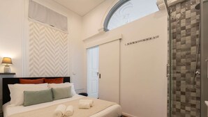 A bedroom with a bed, pillows, a bedside lamp, a shower, and a door. - Cozy Studio Central Porto: A/C and Kitchen (Porto)