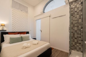 A bedroom with a bed, pillows, a bedside lamp, a shower, and a door.