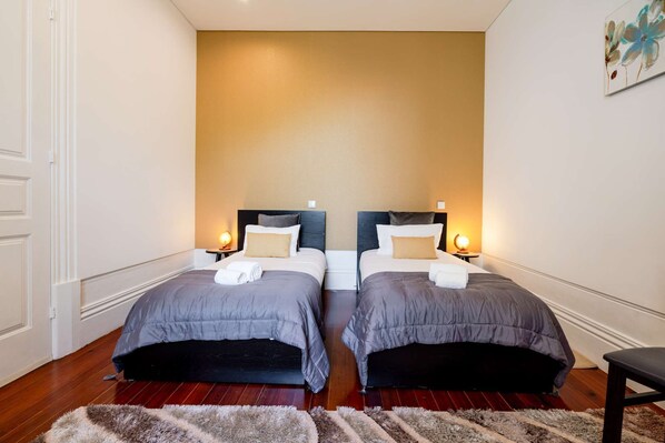 A hotel room with two beds, each with a headboard, bedside lamps, and a fluffy rug.
