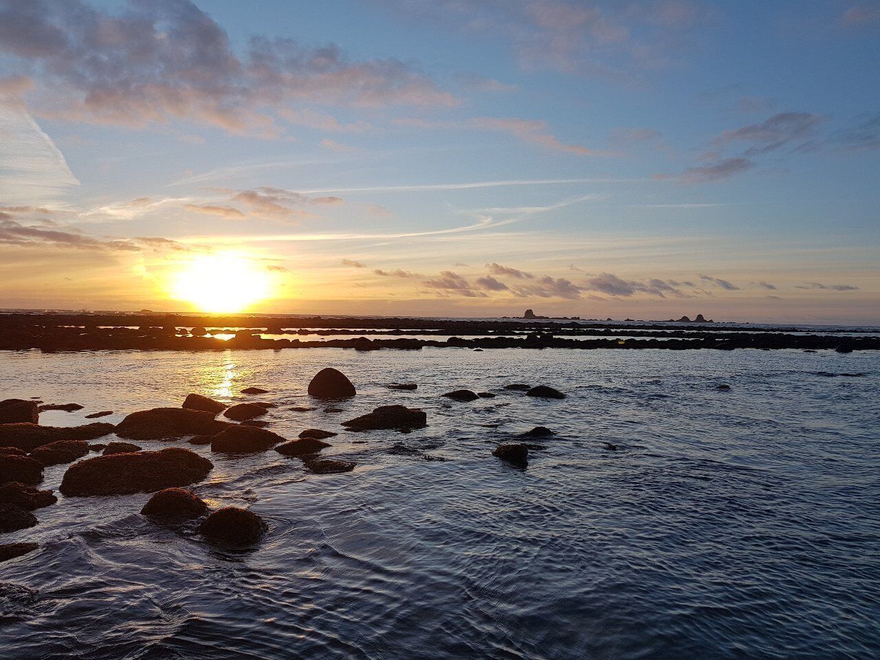 A sunset over a rocky shoreline with calm water.