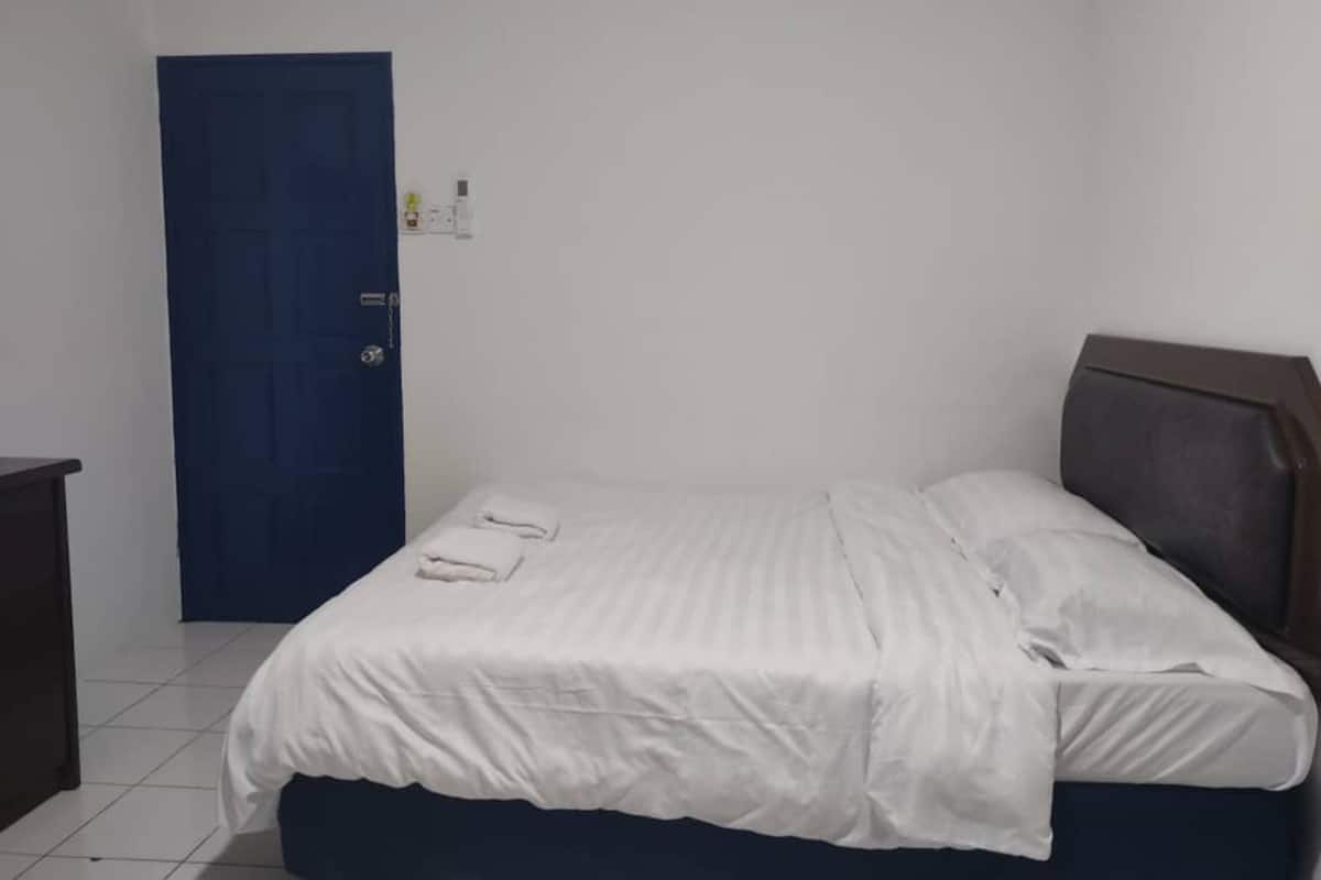 Una habitación pequeña y ordenada con una cama individual, una puerta azul y una mesita.