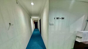 A hallway with a blue carpet, white walls, and a green carpet at the end. A sign on the wall indicates room numbers 101-104. - Hotel O Vaigan Hotel (Bintulu)