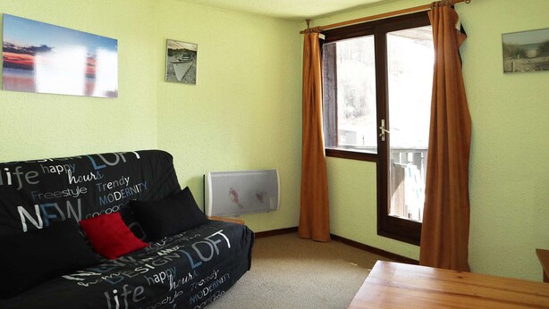 A room with a black sofa, a table, a ceiling fan, and a window with curtains. - Studio 4 pers. direct access slopes, center and south-facing balcony (Les Orres)