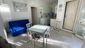 A compact living space with a dining table, chairs, a blue sofa, and a kitchenette. - Duplex la maddalena (Sardegna)