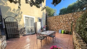 A patio with a table and chairs, a potted plant, and a stone wall. - Duplex la maddalena (Sardegna)