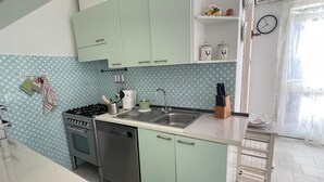 A kitchen with light green cabinets, a stainless steel stove, and a sink. There are kitchen utensils on the counter and a clock on the wall. - Duplex la maddalena (Sardegna)