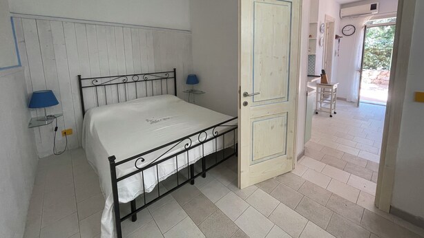 A bedroom with a bed, a nightstand, a lamp, and a door leading to a bathroom. - Duplex la maddalena (Sardegna)