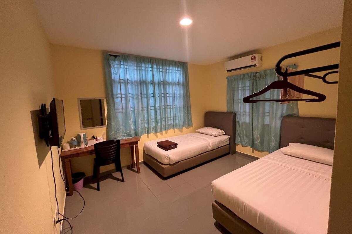 Ein Hotelzimmer mit zwei Betten, einem Schreibtisch, einem Stuhl, einem Fernseher und einer Klimaanlage.