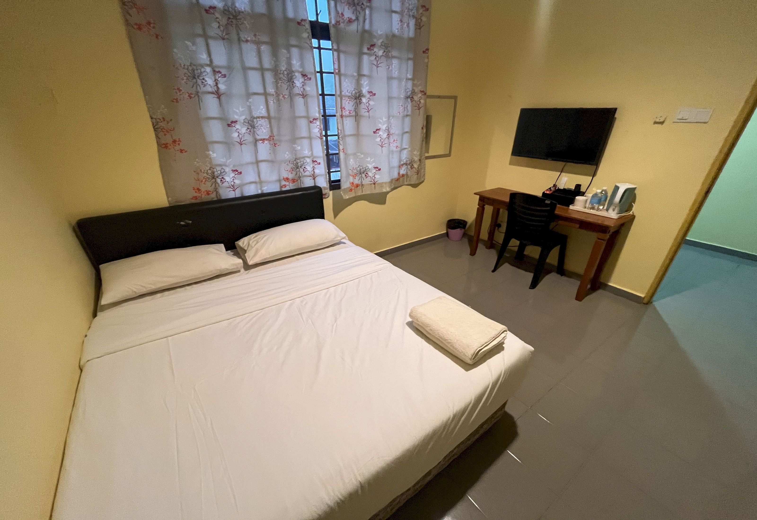 A hotel room with a bed, a desk, a chair, a TV, and a window with curtains.