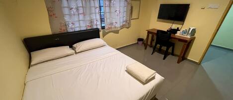 A hotel room with a bed, a desk, a chair, a TV, and a window with curtains.