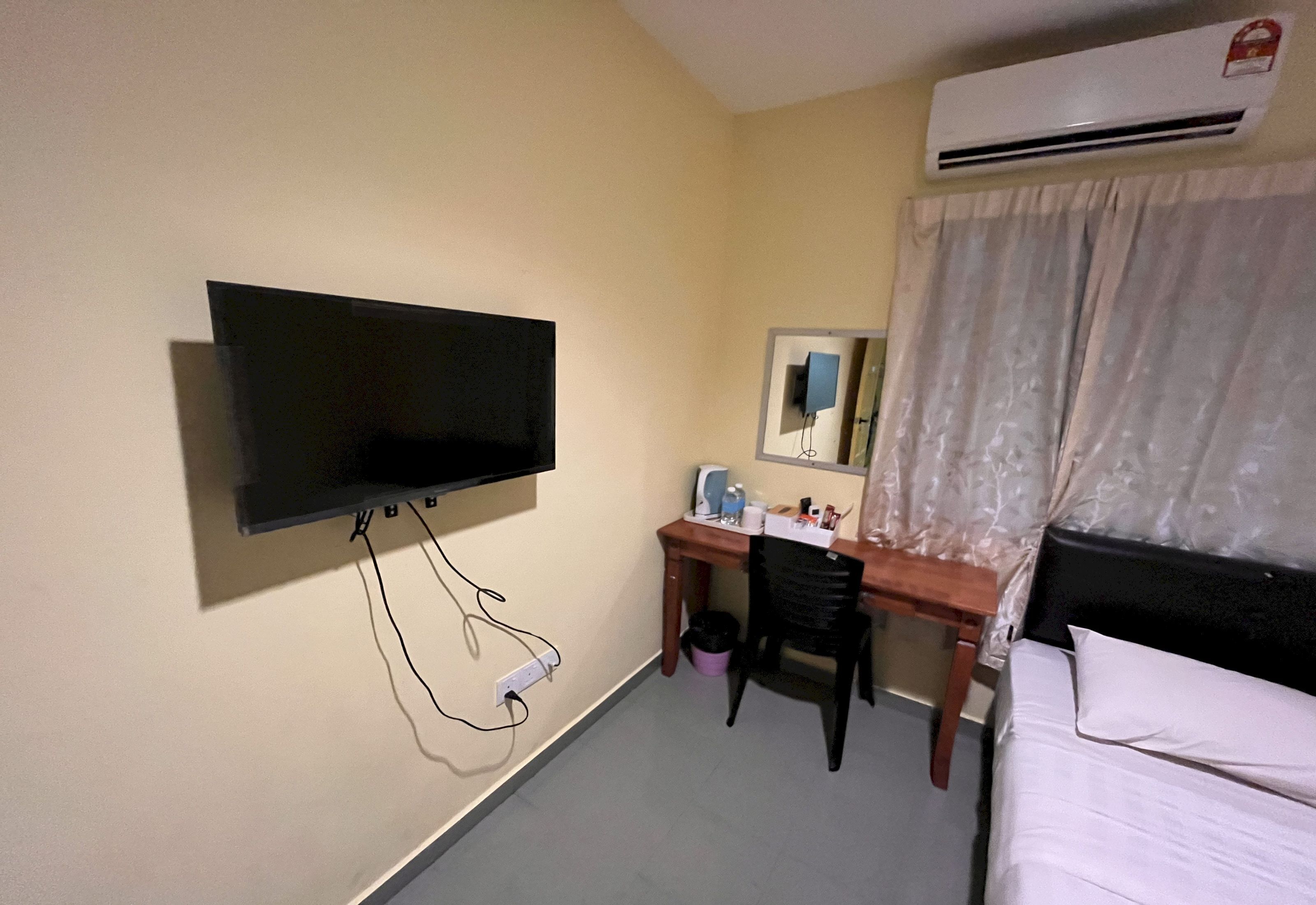 Ein Hotelzimmer mit Flachbildfernseher an der Wand, einem Schreibtisch mit Stuhl, einem Bett und einer Klimaanlage.