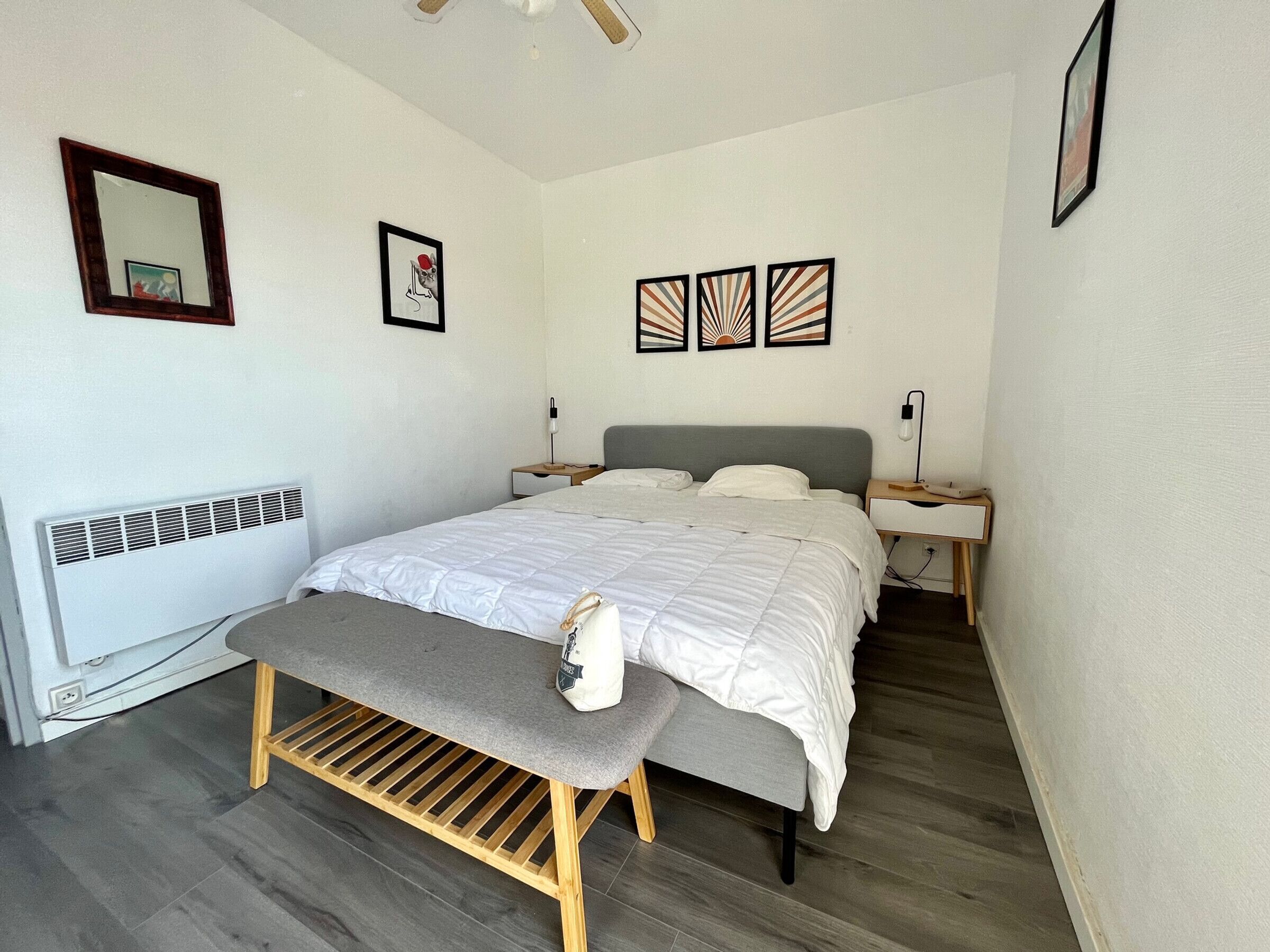 A bedroom with a bed, bedside tables, a bench, a radiator, and wall art.