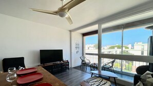 A modern living room with a dining area, large windows, and a ceiling fan.