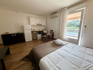 A compact room with a bed, a small kitchenette, a dining table, and a window. - Air-conditioned studio with pool and parking in Saint-Florent (Saint-Florent)