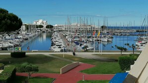 A marina with numerous boats docked, a clear sky, and a building in the background. - Renovated 2-room apartment with pool and parking (Port Camargue)