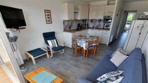 A compact living space with a sofa, a dining table, a TV, and a kitchenette. - Renovated 2-room apartment with pool and parking (Port Camargue)