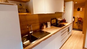 A modern kitchen with white cabinets, a stainless steel sink, wooden countertops, and a wooden ceiling.