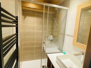 Casa de banho moderna com chuveiro separado por vidro, lavatório branco e espelho.