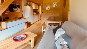 A cozy cabin interior with a wooden staircase, a kitchen area, a dining table, and a sofa.