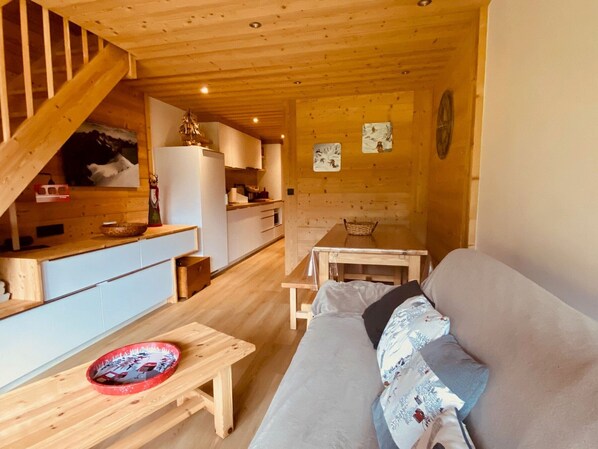 Ein gemütliches Blockhaus-Interieur mit einer Holztreppe, einer Küchenzeile, einem Esstisch und einer Couch.