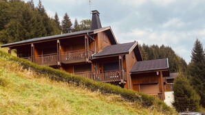 A wooden chalet with multiple balconies, set on a hillside with a forest backdrop.