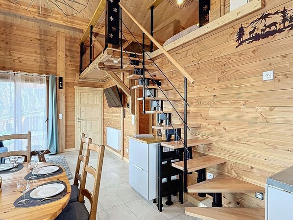 Interior de madera con una escalera espiral, un comedor con mesa dispuesta para dos personas, y una zona de cocina.