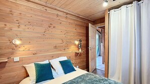 A wooden-paneled room with a bed, two wall-mounted lights, and a door leading to another room. - Comfort chalet 6 pers. with parking and wifi in Le Corbier (Le Corbier)