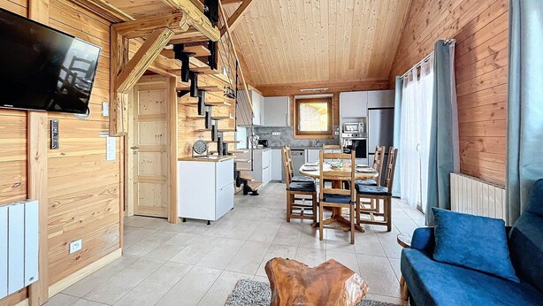 A spacious living area with a wooden interior, a dining table with chairs, a blue sofa, and a kitchen in the background. - Comfort chalet 6 pers. with parking and wifi in Le Corbier (Le Corbier)