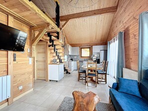 Un salón amplio con detalles de madera, una mesa de comedor con sillas, un sofá azul y una cocina al fondo.