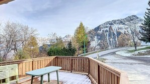 A wooden deck with a table and benches, overlooking a mountain and a road. - Comfort chalet 6 pers. with parking and wifi in Le Corbier (Le Corbier)