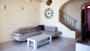 A living room with a beige sofa, a white coffee table, a wall clock, and a staircase with a red door.