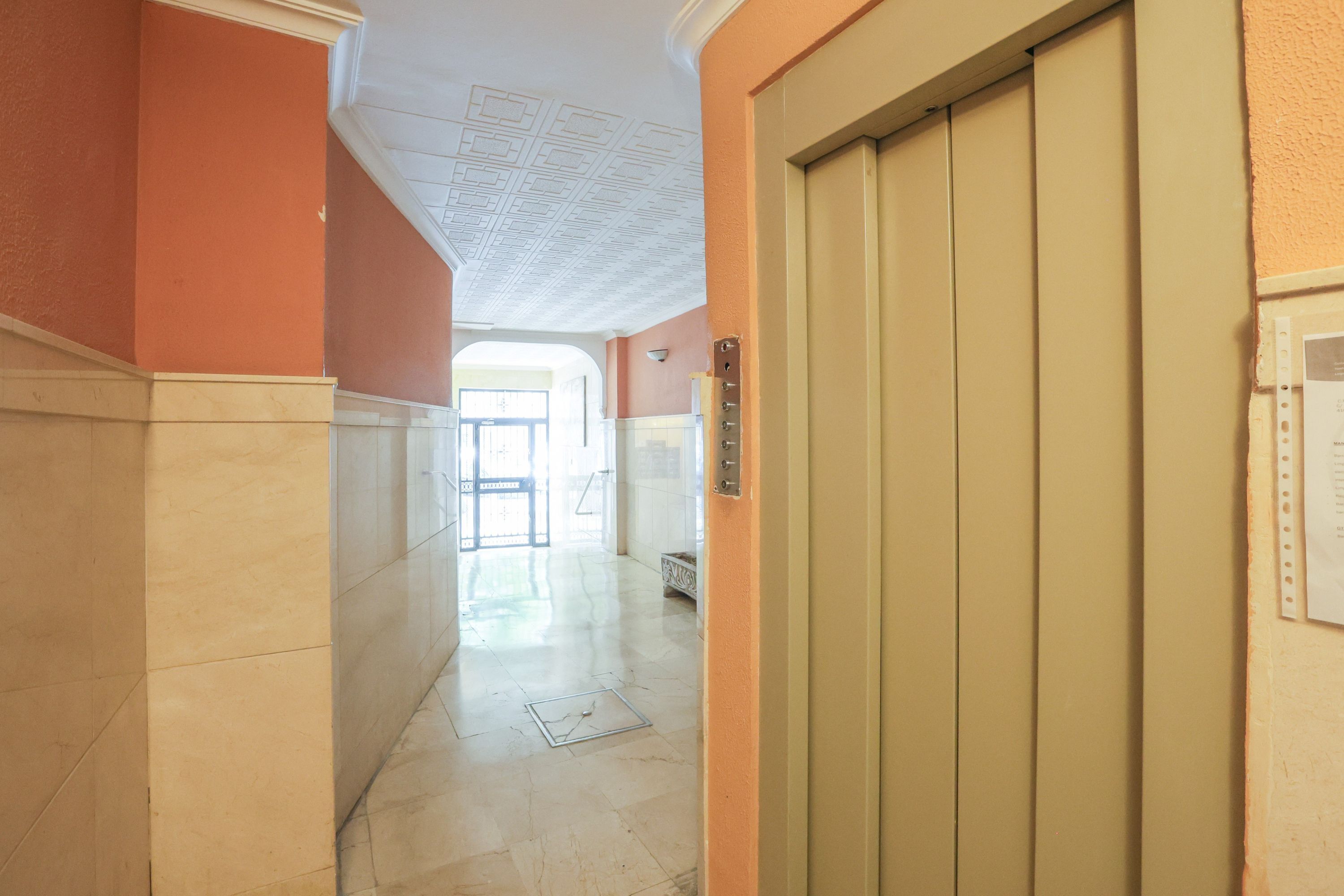 A hallway with a marble floor, a beige elevator, and a door with a light switch.