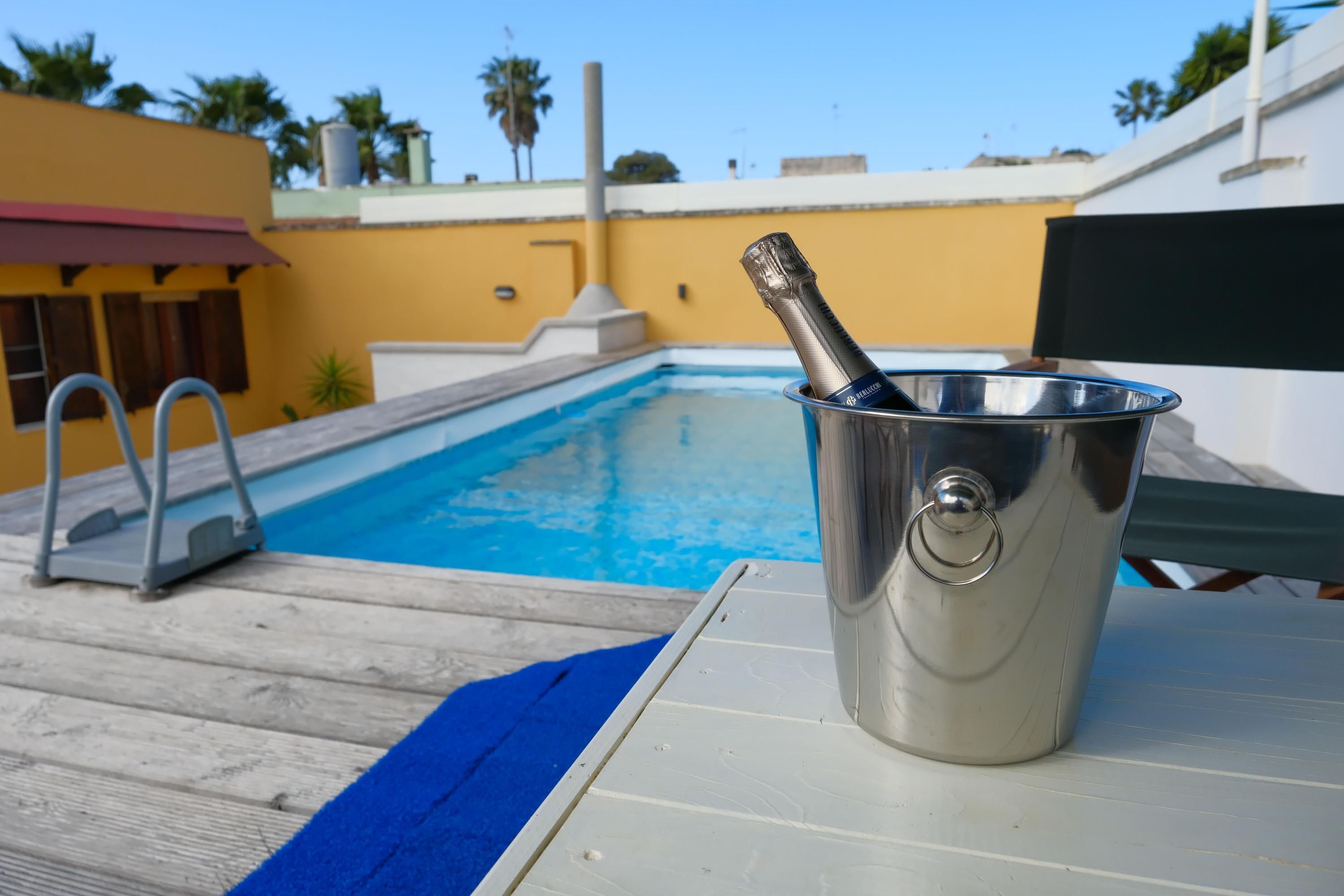 A poolside area with a metal bucket containing a bottle, a pool, and a wooden deck.