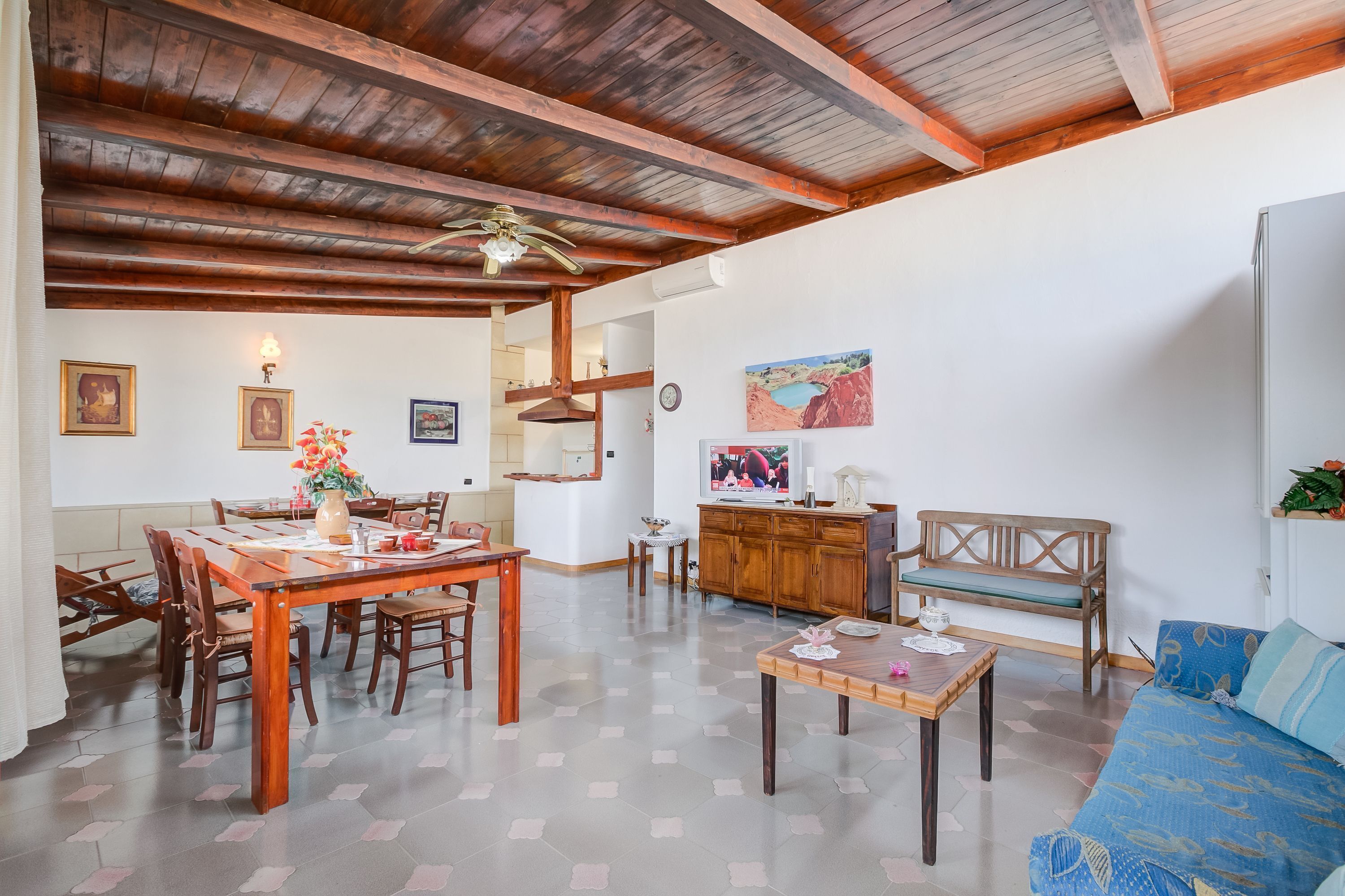 A spacious living area with a wooden dining table, chairs, a sofa, and a television.