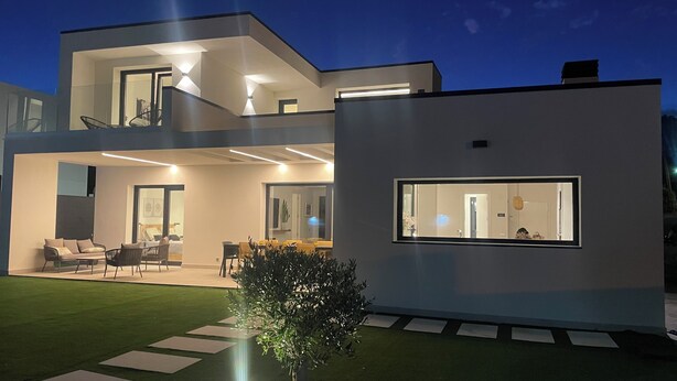 Una casa moderna de dos pisos, con un balcón, un comedor y un gran ventanal en la planta baja.