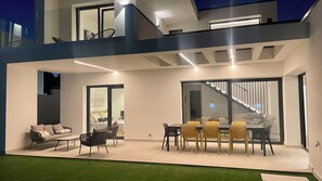 Un área exterior moderna con sala de estar, mesa y sillas, un sofá y una escalera que sube a un nivel superior.