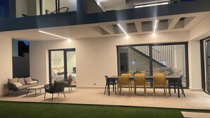 Un espacio moderno para comer al aire libre con una mesa, sillas, un sofá y una escalera que lleva a un nivel superior.