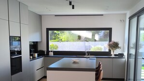 Una cocina moderna con una isla central, electrodomésticos integrados y grandes ventanales que ofrecen vistas al verdor.